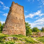 Donjon carré du Weckmund en grès rose vu en contre-plongée depuis la prairie, avec un pan d’enceinte en ruine à droite