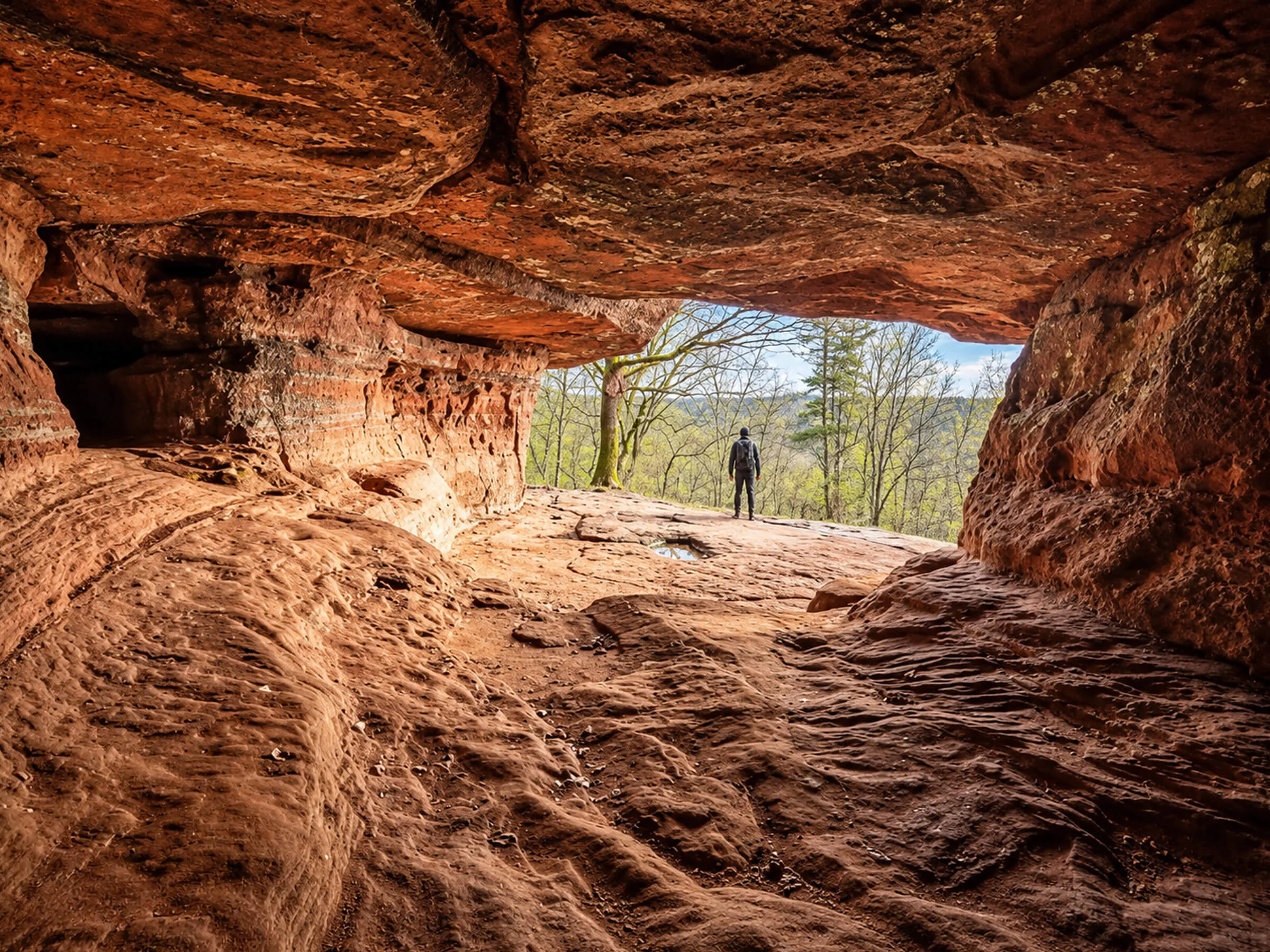 Randonneur à l’entrée d’une grotte de grès rose dans la forêt